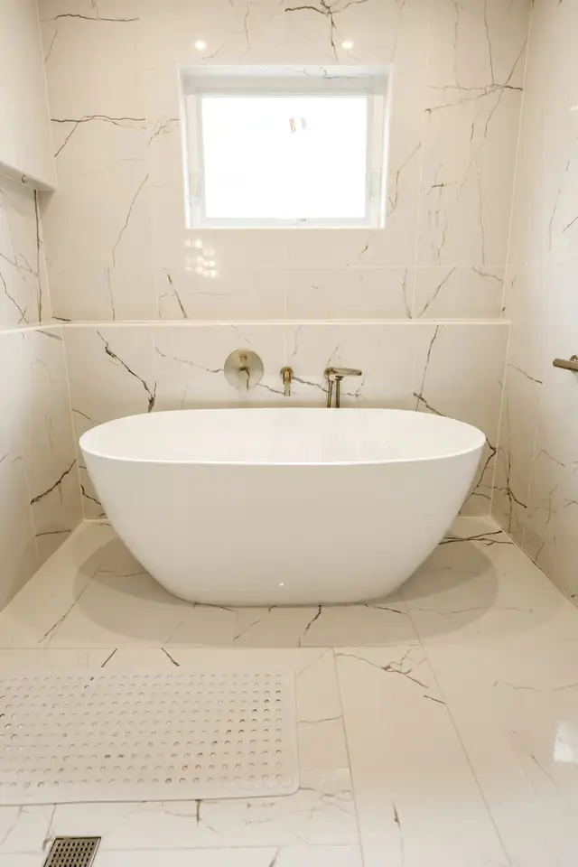 Freestanding tub under a window in a bathroom wrapped in large marble-look tile