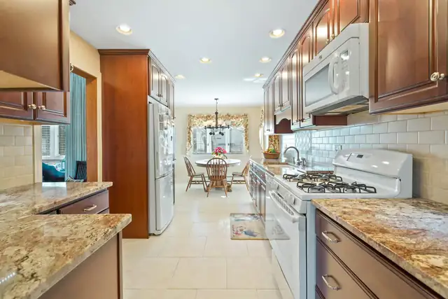 Galley kitchen with cherry cabinets, granite counters, subway tile backsplash and a view into the dining room