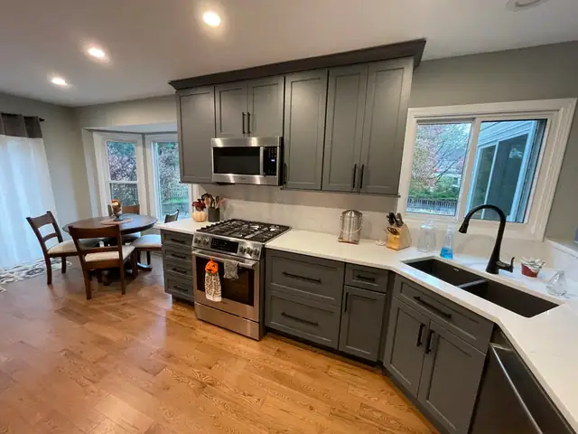 Gray Shaker kitchen with white counters, black faucet and a bay window over the breakfast table