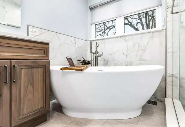 Lindenhurst bathroom with a walnut-stained vanity, freestanding soaking tub and marble-look porcelain wall tile