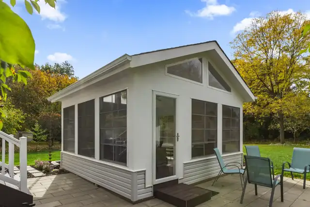 Screen house addition with white siding, gable windows and patio seating on a paver pad