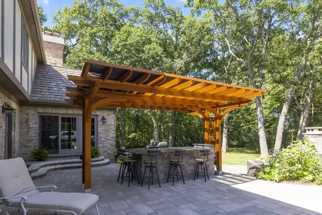 Cedar pergola over a paver patio with a stone outdoor kitchen bar