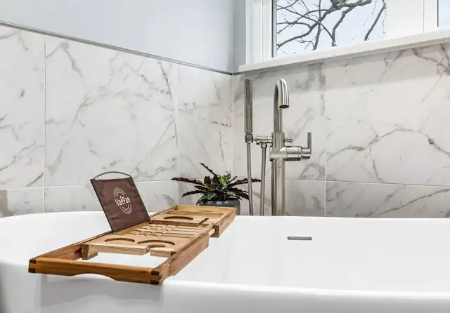 Freestanding tub with a wood bath tray, floor-mounted faucet and marble-look wall tile