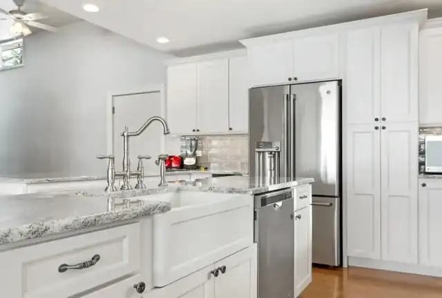 White kitchen with farmhouse sink, granite counters, bridge faucet and stainless refrigerator